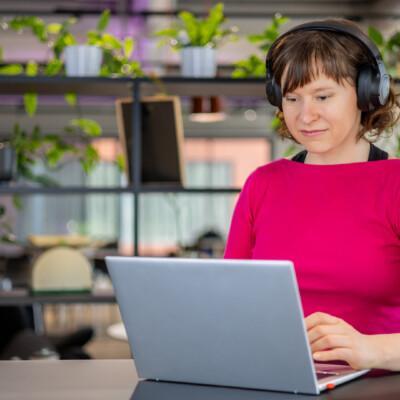Nainen istuu kuulokkeet korvilla ja kannettava tietokone edessään. Hän opiskelee digiosaava myyjä verkkokoulutuksessa.