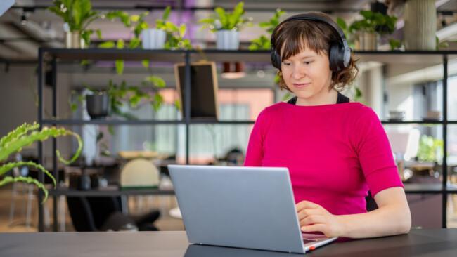 Nainen istuu kuulokkeet korvilla ja kannettava tietokone edessään. Hän opiskelee digiosaava myyjä verkkokoulutuksessa.