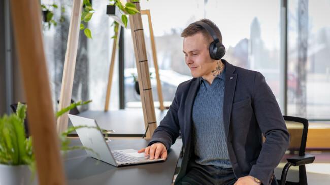 Mies kannettavalla tietokoneella, kuulokkeet päässä ajasta ja paikasta riippumattomissa verkko-opinnoissa Suomen Yrittäjäopistossa